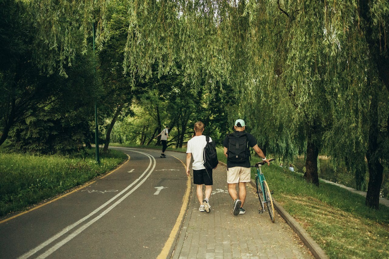 Two people walk, one carrying a backpack and the other his bike.